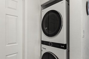 A stacked washer and dryer unit in a room with white walls and a door. - Luxury TPC | Heated Pool | Barrett-Jackson+Parking (Scottsdale)