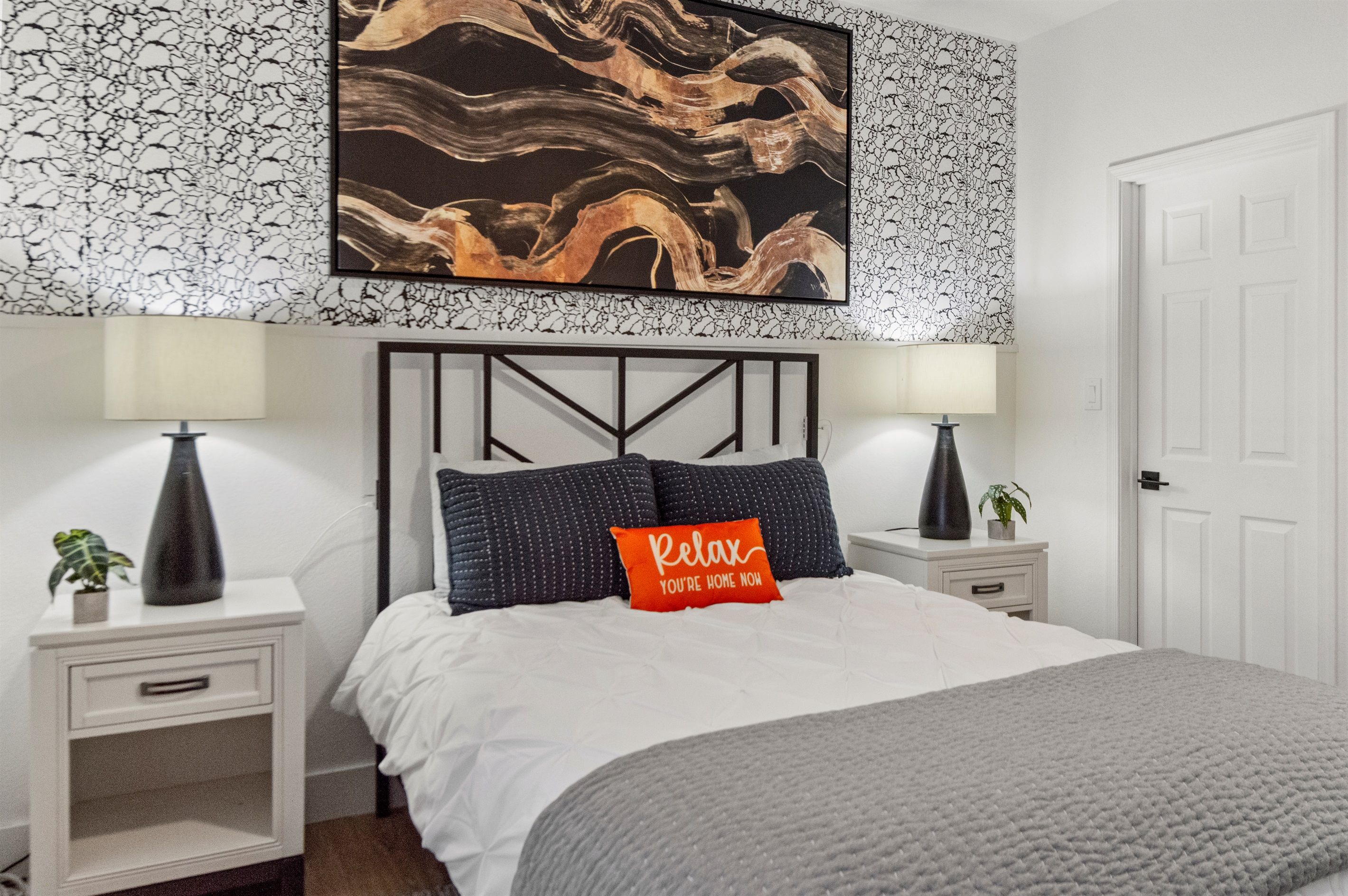 Een slaapkamer met een bed, twee nachtkastjes, een wanddecoratie en een deur.