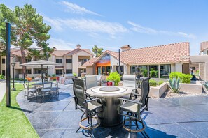 A patio with a round table and chairs, surrounded by a landscaped garden and a building with a tiled roof. - WestWorld + TPC | Heated Pool + Hot Tub (Scottsdale)