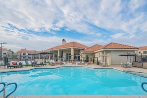 Ein Swimmingpool mit Liegestühlen und Sonnenschirmen, umgeben von Gebäuden mit roten Ziegeldächern.