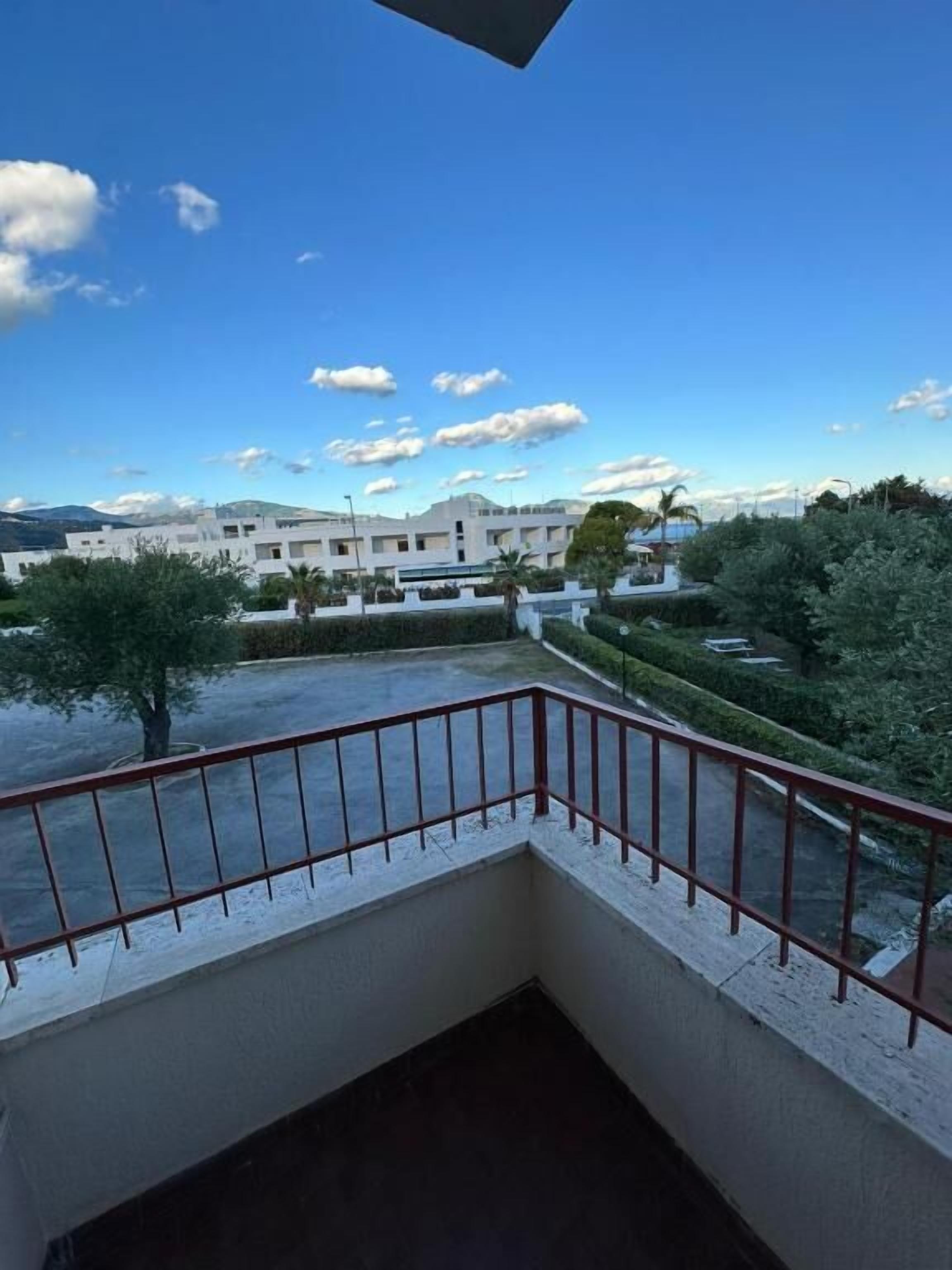 A balcony with a red railing overlooking a landscaped area with trees and a building in the background.