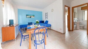 Una habitación con una mesa de comedor, sillas, un sofá, una televisión y un baño visible a través de una puerta abierta.