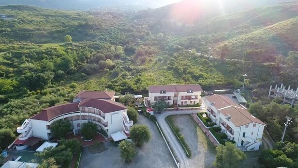 Un gran edificio con varias alas, rodeado de exuberante vegetación y colinas.