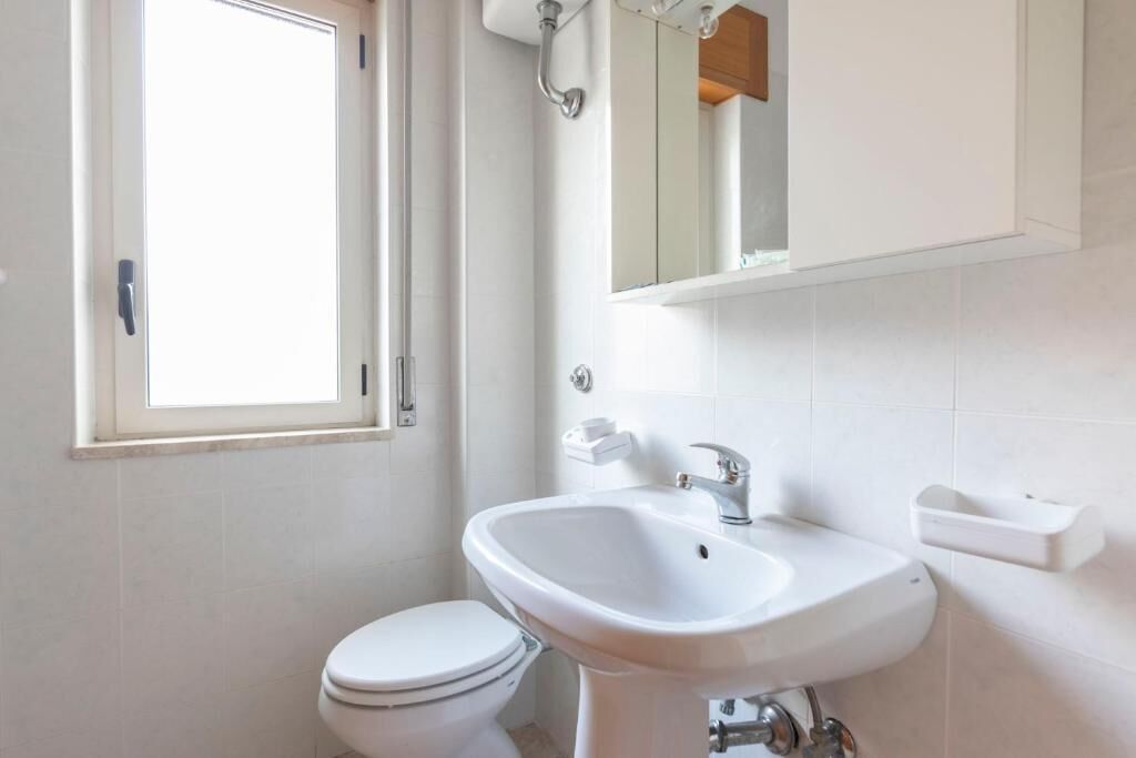 Een badkamer met een toilet, een wastafel, een spiegel en een raam.