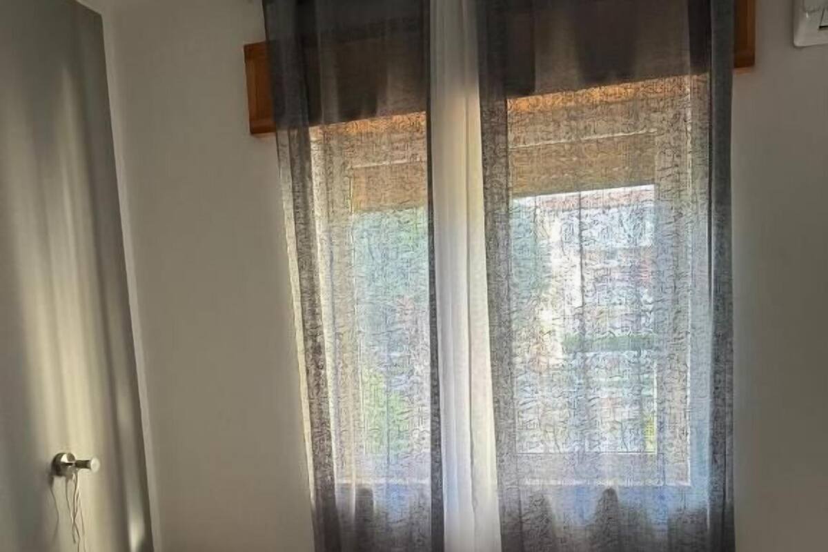 Hotellihuone, jossa on sänky, yöpöytä, ikkuna verhoilla ja näkymä ulos.