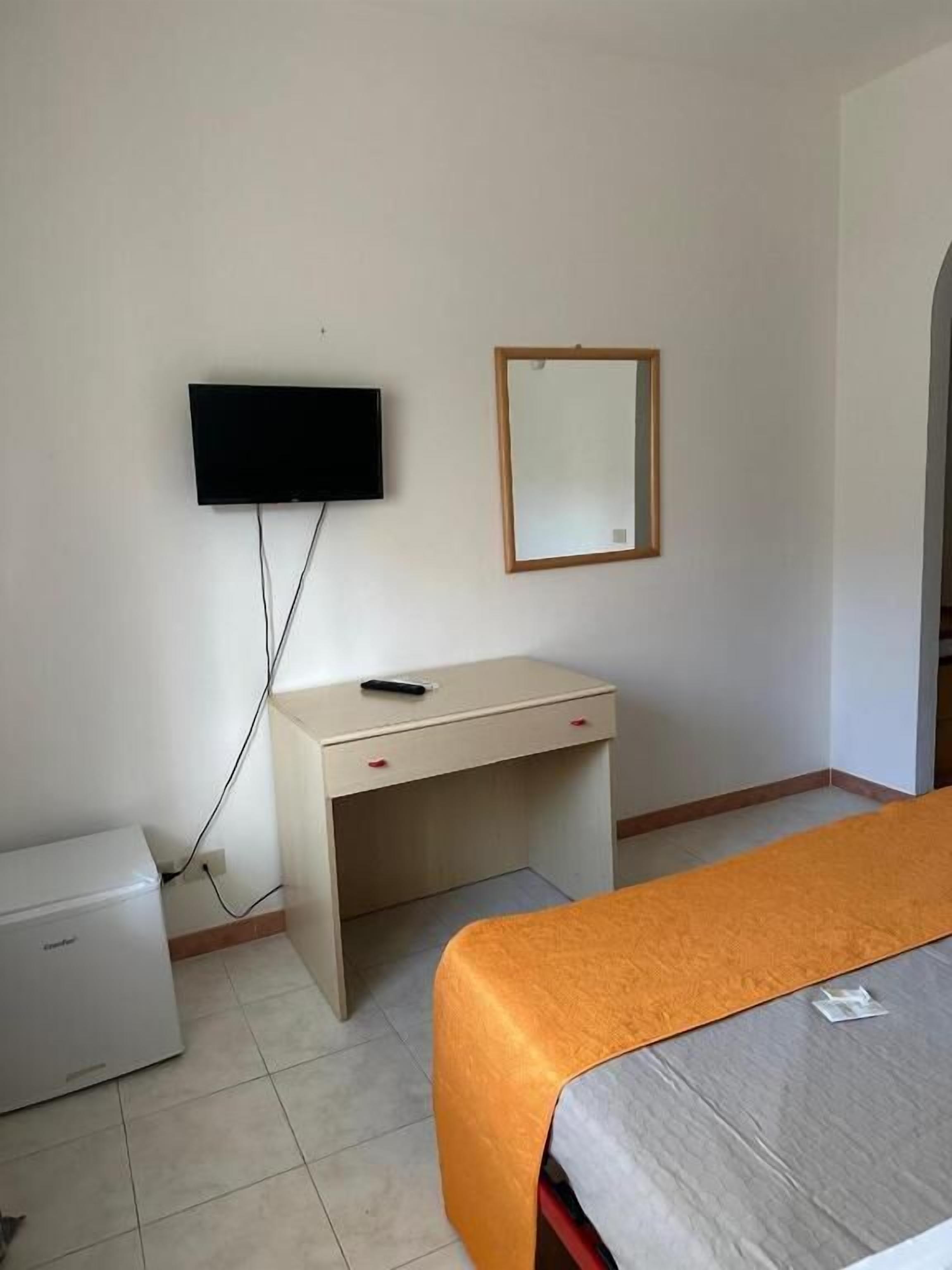 Una habitación de hotel con cama, escritorio, televisión montada en la pared y refrigerador.