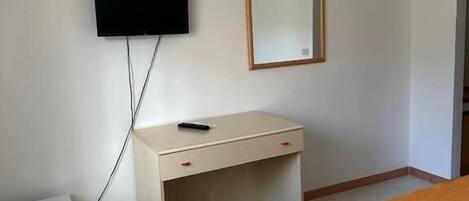 Una habitación de hotel con cama, escritorio, televisión montada en la pared y refrigerador.