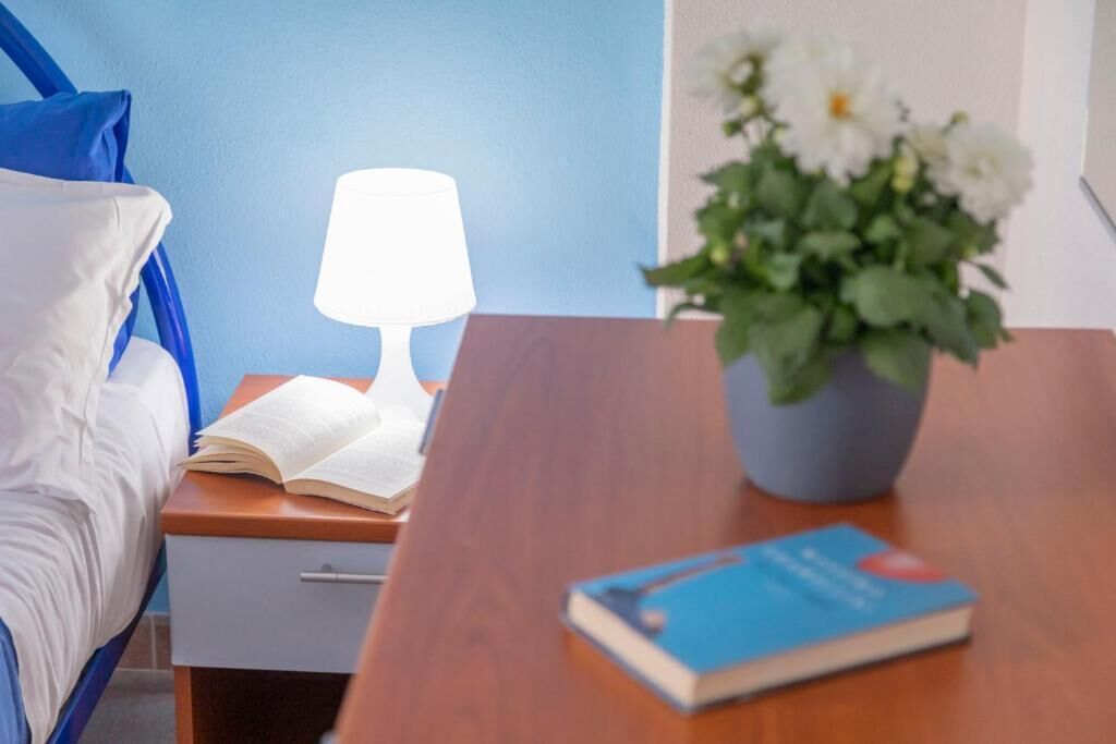 A bedroom with a bed, a bedside table with a lamp, a book, and a potted plant.