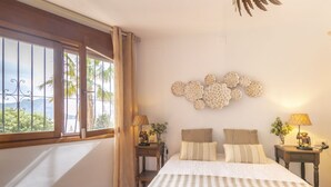 A bedroom with a large bed, a window with curtains, a wall-mounted decorative piece, and two bedside tables with lamps. - Villa Wioleta - Costa CarpeDiem (Benissa, Alicante)