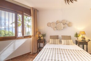 A bedroom with a large bed, a window with curtains, a wall-mounted decorative piece, and two bedside tables with lamps. - Villa Wioleta - Costa CarpeDiem (Benissa, Alicante)