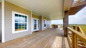 Une véranda couverte avec une terrasse en bois, de grandes fenêtres et une vue sur le paysage.