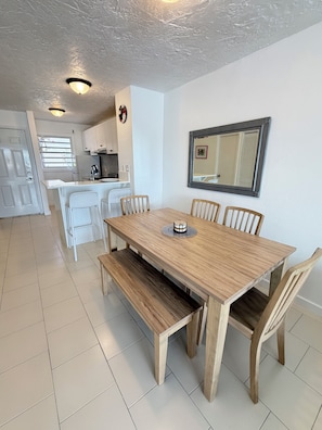 A dining area with a wooden table and chairs, a kitchen in the background, and a white ceiling. - Stylish Waterfront Villa w/ Dock & Sun Deck (Jolly Harbour)