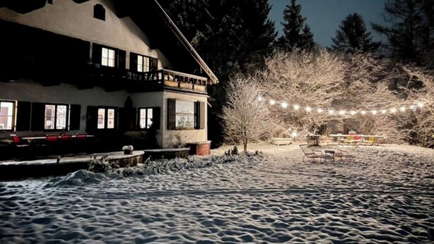 Ein Gebäude mit einem Balkon, verschneitem Gelände und Lichterketten.