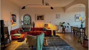 Ein Wohnzimmer mit einem roten Sofa, einem weißen Sessel, einem Holztisch und einem großen Fenster.