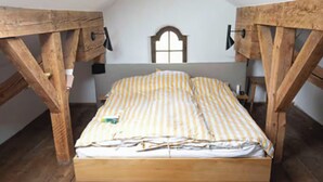 Ein Bett mit Holzbettgestell und einem gestreiften Bettbezug in einem Zimmer mit freiliegenden Holzbalken und einem Fenster mit weißem Rahmen.