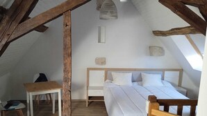 Et soveværelse med træloft, en seng med hvide sengetæpper, et lille bord og en hængende lampe.