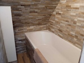 Een badkamer met een betegelde muur, een badkuip en een houten vloer.