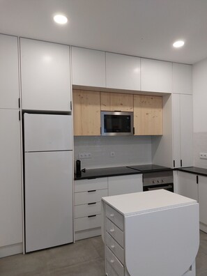 Eine moderne Küche mit weißen Schränken, einem Edelstahl-Kühlschrank, einer Mikrowelle und einem Einbauofen.