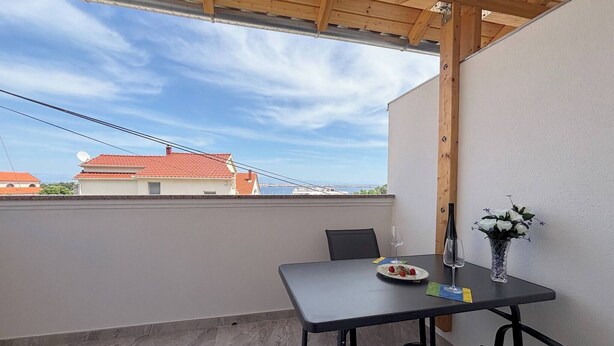A balcony with a table, chairs, a vase with flowers, and a view of buildings. - Sea View Apartment Marijana (Preko)