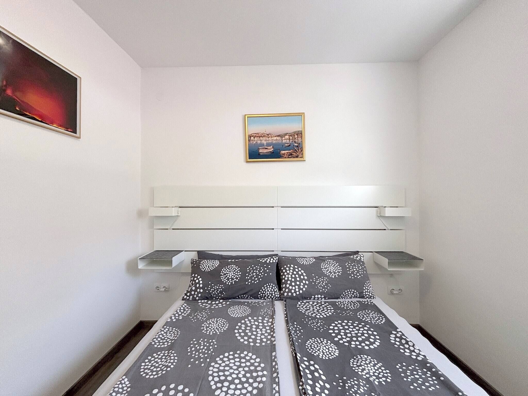 A small, neatly organized bedroom with a bed, a nightstand, a shelf, and a framed picture on the wall.