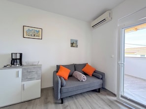 A modern living room with a grey sofa, orange cushions, a coffee maker, and a small cabinet. - Sea View Apartment Marijana (Preko)
