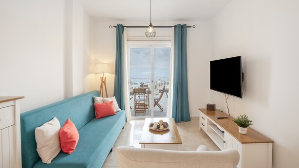 Ein Wohnzimmer mit Sofa, Couchtisch, Fernseher und Balkonblick.