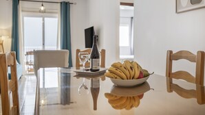 Ein Esstisch mit Obstschale und Weinflasche, Holzstühle, ein Glas und ein Fernseher an der Wand.