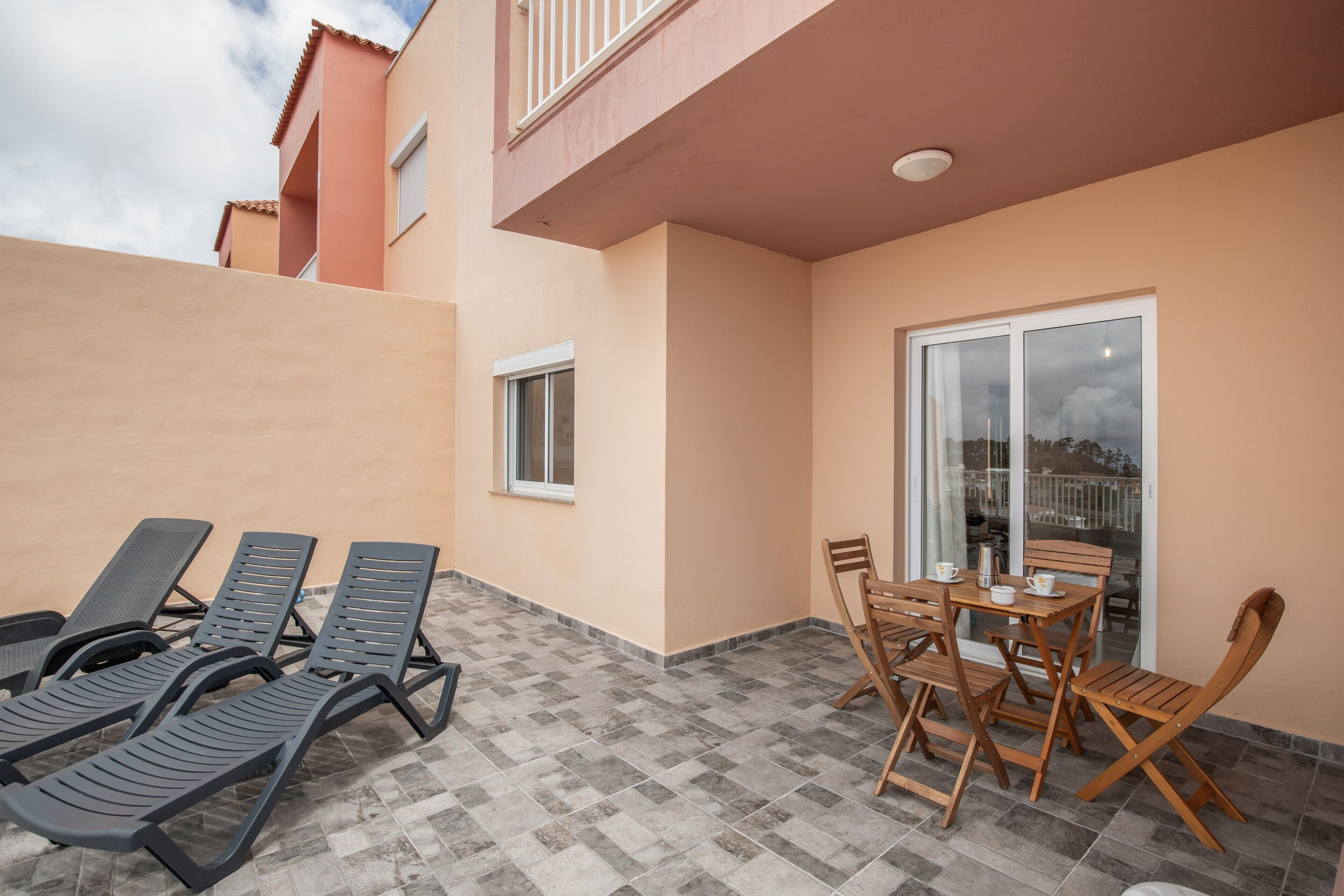 Un balcone con poltrone da relax, un tavolo e sedie, e una porta scorrevole in vetro.