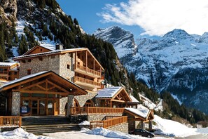A mountain lodge with stone and wood construction, multiple balconies, and a view of snow-covered peaks. - Appart Ski aux Pieds | Terrasse + Accès piscine (Pralognan-La-Vanoise)