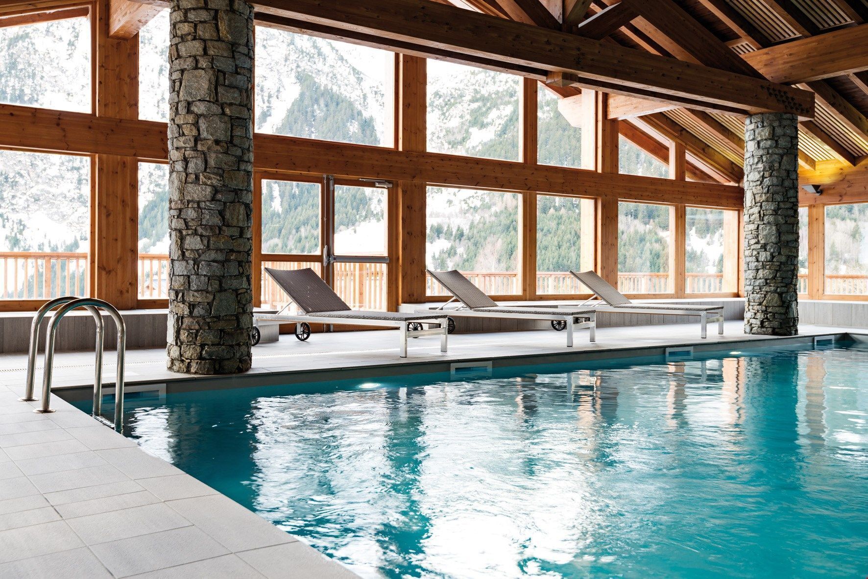 Une piscine intérieure agrémentée de piliers en pierre, de poutres en bois et de grandes fenêtres.