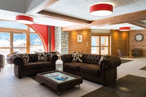 A spacious lobby with leather sofas, a coffee table, and a clock on the wall. - Appart Ski aux Pieds | Terrasse + Accès piscine (Pralognan-La-Vanoise)