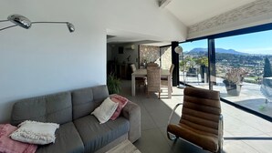 A modern living room with a sofa, armchair, and dining area, featuring a large window with a city and mountain view. - 🌴 SPECIAL SUMMER CLOSING SALE: 30% off from August 22 to August 29 🌴 (Ollioules)