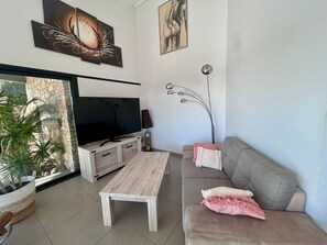 A modern living room with a flat-screen TV, a wooden coffee table, a grey sofa with pink cushions, and a floor lamp. - 🌴 SPECIAL SUMMER CLOSING SALE: 30% off from August 22 to August 29 🌴 (Ollioules)