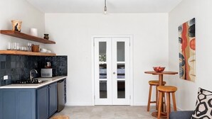 A compact kitchen with dark blue cabinets, a black tiled backsplash, a white door, and a small dining area with stools.