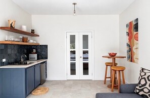 Una cocina compacta con armarios azul oscuro, salpicadero de azulejos negros, una puerta blanca y un pequeño comedor con taburetes.