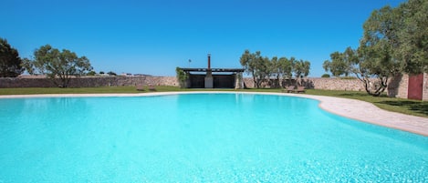 En klar, blå swimmingpool med en stenvæg og træer i baggrunden.