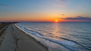 Een strand met een zonsondergang, golven en een heldere lucht.