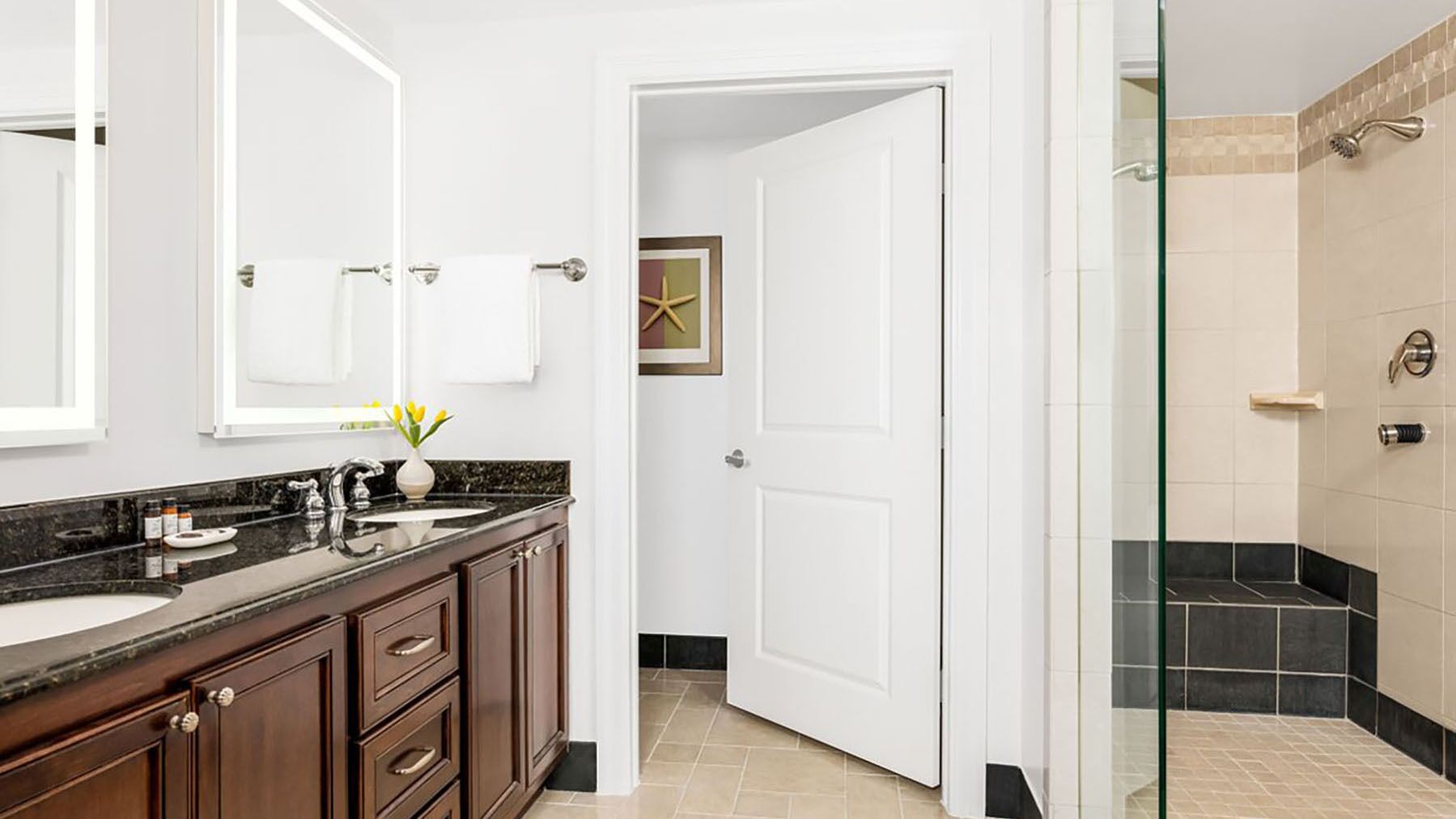A modern bathroom with a double sink vanity, a large mirror, and a glass shower enclosure.