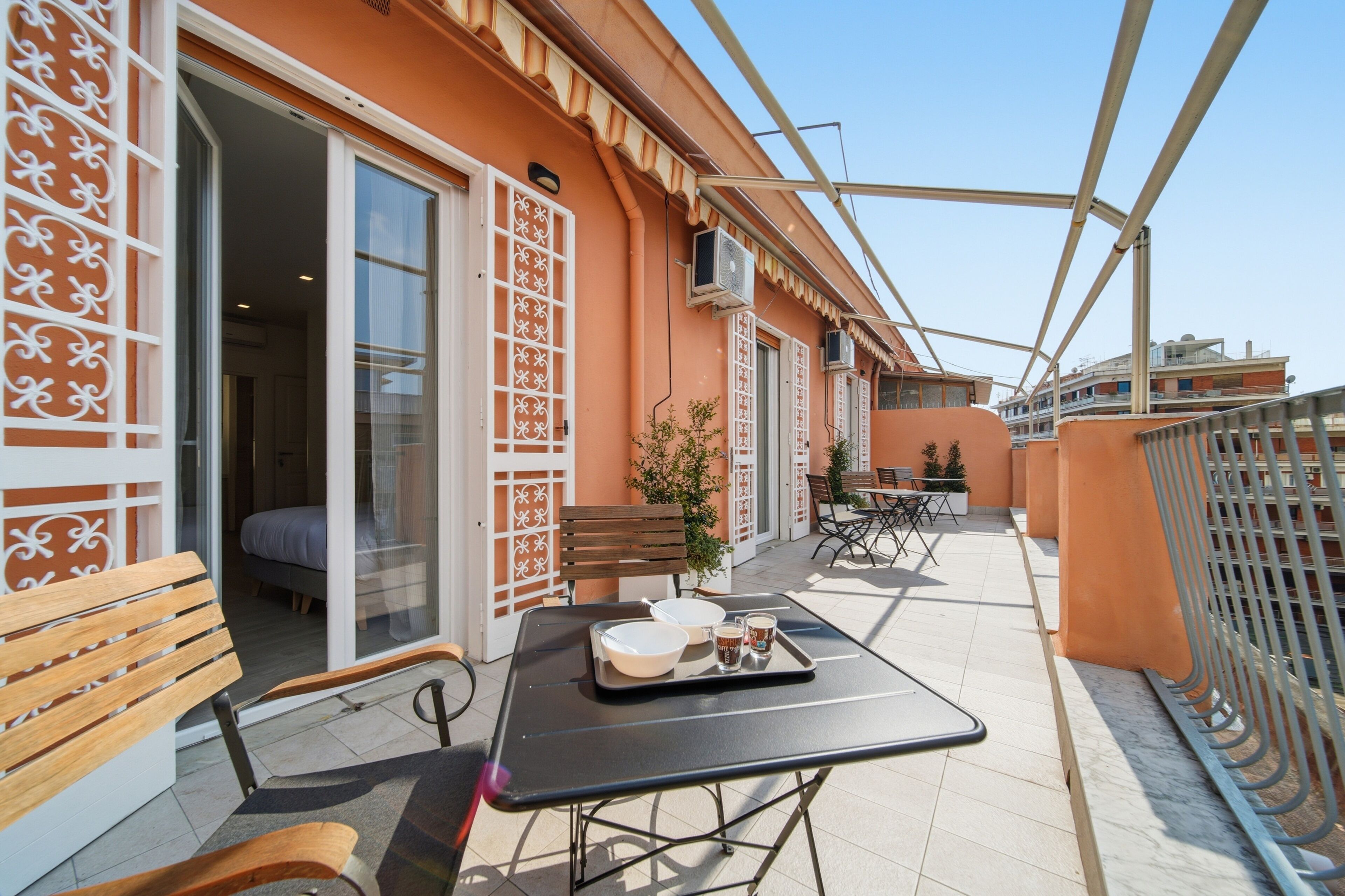 Un balcón con una mesa para dos, una banca y una puerta que da a una habitación.