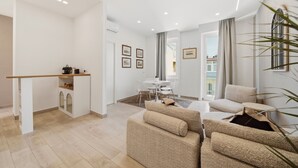 A modern living room with a sofa set, a dining area with a table and chairs, and a kitchen area with a counter and cabinets. - Alpha Domus 15 (Naples)