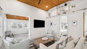 A modern living room with a flat-screen TV, a sofa, a chair, a coffee table, and a ceiling fan. - Steps to Beach Access w/ Screened Porch (Santa Rosa Beach)