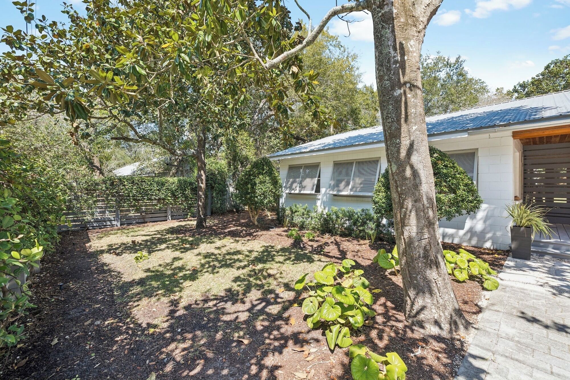 A house with a covered porch, a fenced yard, and a large tree.