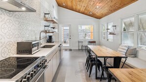 A modern kitchen with a wooden ceiling, white walls with patterned wallpaper, a built-in stove, and a dining area with a table and chairs. - Steps to Beach Access w/ Screened Porch (Santa Rosa Beach)