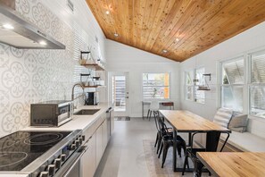 Eine moderne Küche mit Holzboden, weißen Wänden mit ornamentalem Tapetenmuster, einem eingebauten Herd und einem Essbereich mit Tisch und Stühlen.