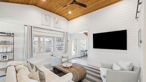 A modern living room with a wooden ceiling, white walls, a large TV, and a sofa. - Steps to Beach Access w/ Screened Porch (Santa Rosa Beach)