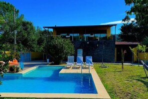 A modern building with a swimming pool, outdoor seating, and a clear blue sky.