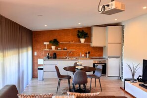 A modern living room with a dining area, a kitchen with brick walls, and a projector.