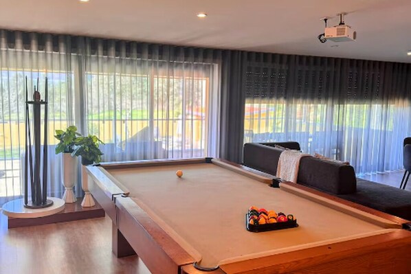 A pool table with balls, a sofa, and a projector in a room with large windows.
