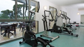 Ein Fitnessstudio mit unterschiedlichen Trainingsgeräten, großen Fenstern und Blick auf Bäume.