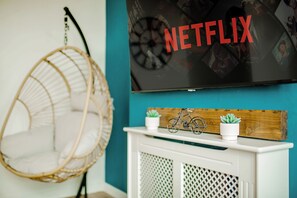 A room with a hanging chair, a white cabinet, and a wall-mounted television displaying the Netflix logo. - Blue Serenity Central Oasis | Free Parking | 10PPL (Sheffield)
